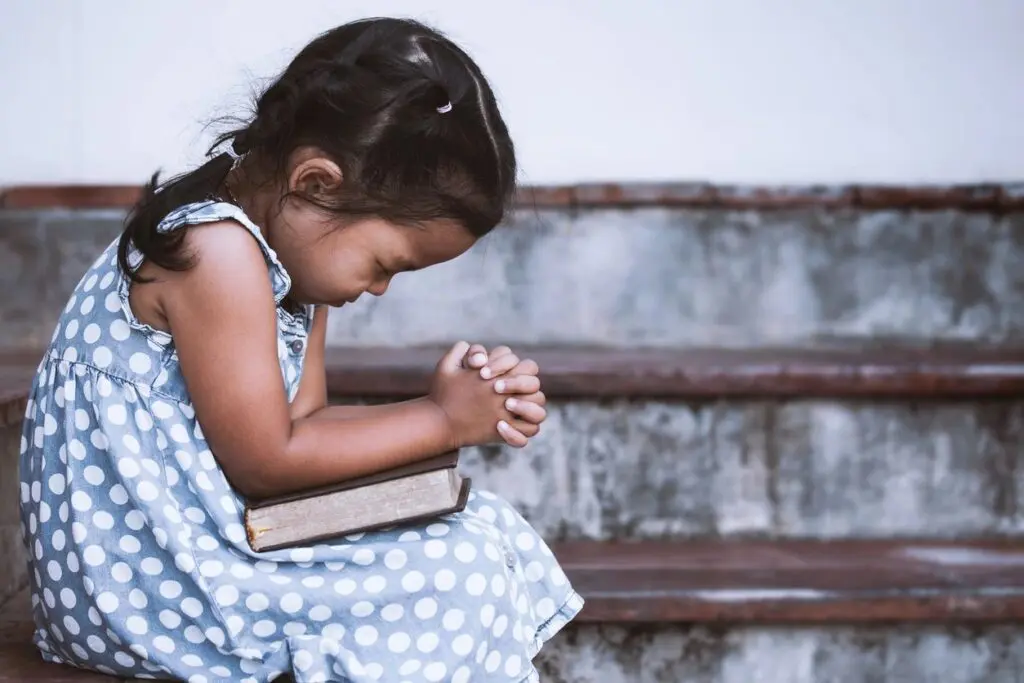 A little girl sitting on the steps holding her hands together.